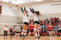 Two IUK volleyball players block an opponent's spike.